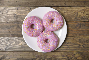 Aerial view of a plate of ring donuts with pastel pink frosting and sprinkles on a rustic wooden table background
