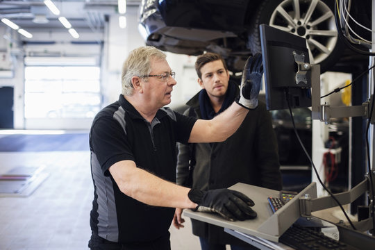 Senior mechanic showing computer monitor while discussing with customer at repair shop