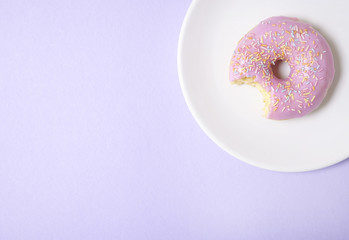 A ring doughnut with pastel pink frosting and sprinkles on a purple background, with a bite missing...