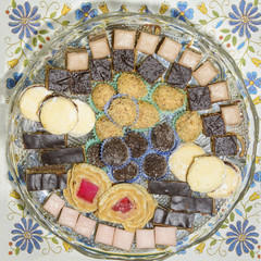 Small cookies on a glass cake stand. Cake roll with jelly, sandwich cookies, raffaello balls...