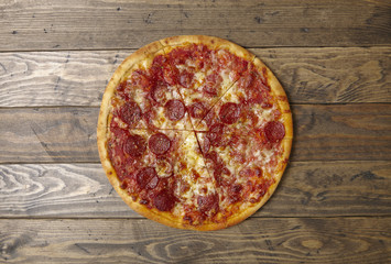 A whole, cooked and sliced peperoni pizza on a rustic wooden background