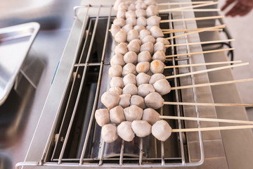 Close up scene : grilled pork meatball skewers on electric roaster 
Thai meat ball with bamboo stick, cooking food sold by vendors in a street or other public location for immediate consumption