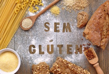 Gluten free flour and cereals millet, quinoa, corn flour polenta, brown buckwheat, basmati rice and pasta with text gluten free in Portuguese language with wooden spoon on brown wooden background © luciepeclova