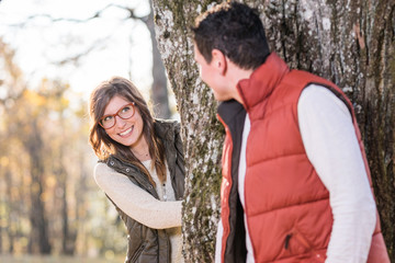 Junge lachende Frau, versteckt sich hinter einem Baum vor ihrem