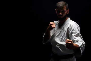 Karate man in a kimono in fighting stance on a black background