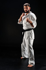 Karate man in a kimono in fighting stance on a black background © amixstudio