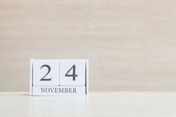 Closeup surface white wooden calendar with black 24 november word on blurred brown wood desk and wood wall textured background with copy space , selective focus at the calendar