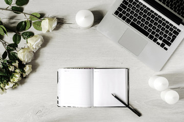 Workplace in modern style with laptop, diary, white candles, roses and wooden desk. Flat lay