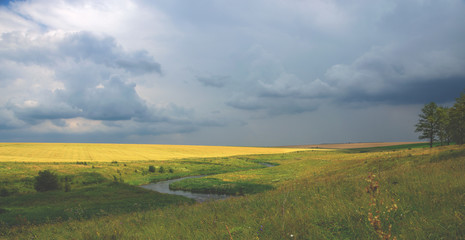 Obraz premium Cloudy summer landscape with river and wheat field