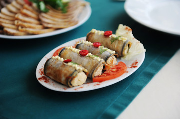 Eggplant rolls on a white plate. Served on a table with a green tablecloth in a restaurant