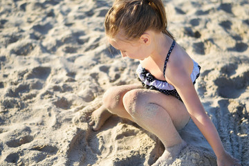 Adorable little girl playing with sand at the beach in summer