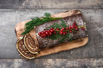 Chocolate yule log christmas cake with red currant on wooden background.copyspace
