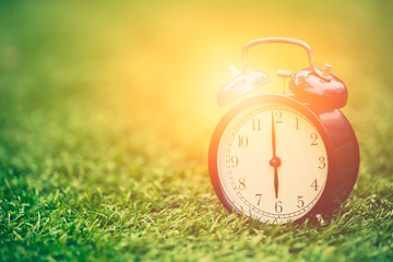 times retro clock lay on green grass nature with sun light face timed at 6 o'clock morning time for background or postcard.