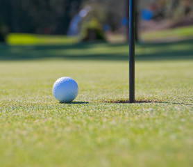 Golf ball on green with flag. Shallow depth of field. Focus on the ball.