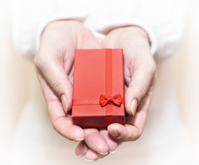 Hands of a woman showing a gift: little red box with a ribbon. Selective focus.