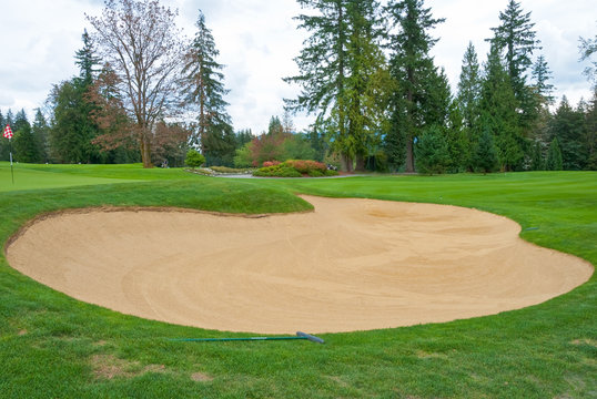 Sand bunker on the golf course with green grass and trees.