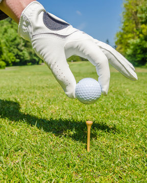 hand placing golf ball on tee over beautiful golf course with blue sky