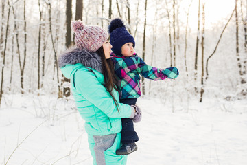 Fototapeta na wymiar happy mother holding baby girl on the walk in winter snowy forest