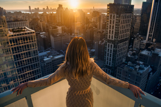Rich woman enjoy the sunset standing on the balcony at luxury apartments in New York City. Luxury life concept. Succesful B.businesswoman relax.