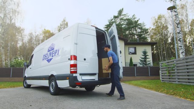 Delivery Man Takes Cardboard Boxes Out of His Cargo Van. In a Suburban Area. Sunny Autumn with Yellow Birches and Pines is on the Background. Shot on RED Cinema Camera in 4K (UHD).