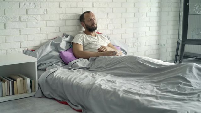 Sad, unhappy man lying on bed at home 
