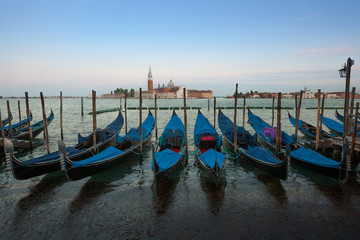 Fototapeta na wymiar Gondolas moored by Saint Mark square with San Giorgio di Maggiore church in the background - Venice, Venezia, Italy.