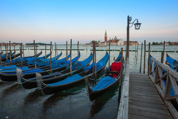 Fototapeta na wymiar Gondolas moored by Saint Mark square with San Giorgio di Maggiore church in the background - Venice, Venezia, Italy.