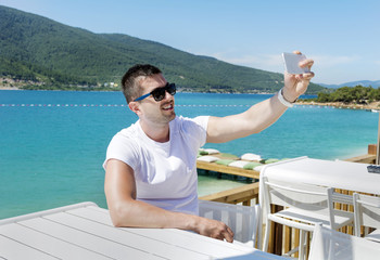 handsome young man taking selfie with his smart phone at the beach.Summer holiday concept