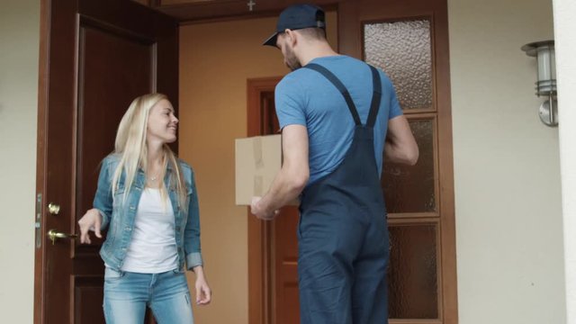 Happy Homeowner Opens Door To Delivery Man and Receives Parcel after Signing on Electronic Signature Device. Shot on RED Cinema Camera in 4K (UHD).