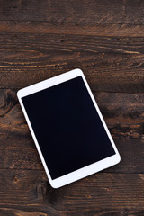 White digital tablet with black screen on wooden table