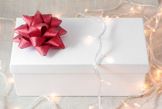 White gift box with red bow and ribbon with garland and many lights
