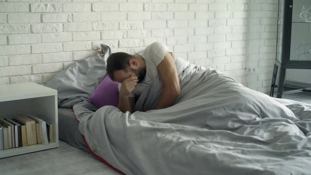Young man waking up from sleep on bed at home
