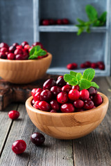 Fresh juicy cranberries in a bamboo bowl on the old wooden background. Selective focus.