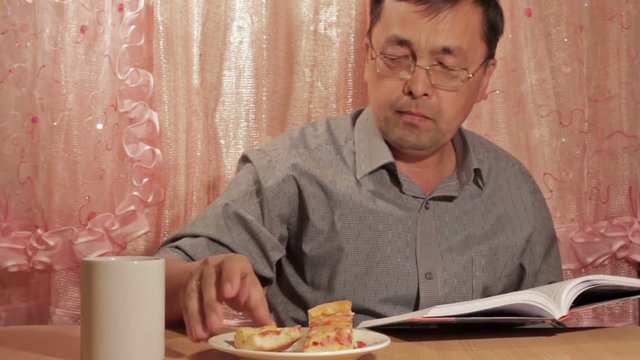 Asian man eating pie at home and reading a book