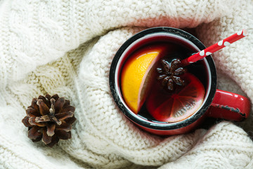 Christmas and winter traditional hot beverage. Mulled wine in red mug with spice wrapped in warm green scandinavian sweater.