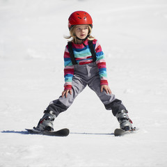 Happy child girl enjoying vacation in winter resort. Little girl skiing in mountains. Active sportive toddler wearing helmet learning to ski. Winter sport for family. Skier racing in snow.