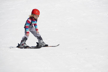 Fototapeta na wymiar Happy child girl enjoying vacation in winter resort. Little girl skiing in mountains. Active sportive toddler wearing helmet learning to ski. Winter sport for family. Skier racing in snow.