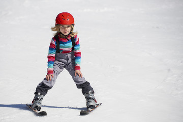 Fototapeta na wymiar Happy child girl enjoying vacation in winter resort. Little girl skiing in mountains. Active sportive toddler wearing helmet learning to ski. Winter sport for family. Skier racing in snow.