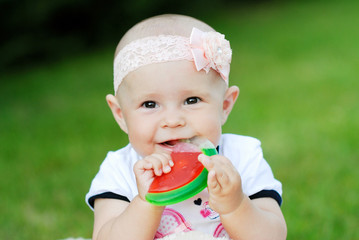 cheerful child with bow on her head chewing on a toy in the form