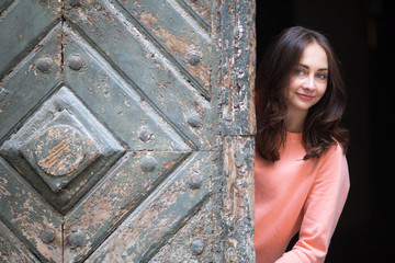 Fototapeta premium Young brunette girl posing near an ancient wooden gate.