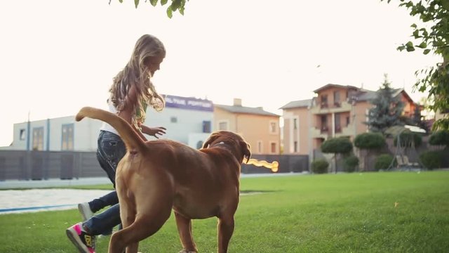 A dog is running with a bone in its mouth together with little European girls cross the yard. Outdoors activities. Family time. Friends forever. Children portrait.