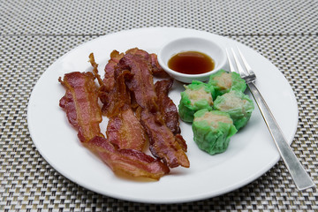 Closeup of fried bacon strips on white plate.