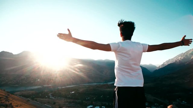 young Asian male reaching to the top of the mountain area, standing on top of a mountain, hands raised, awareness of success, slow motion