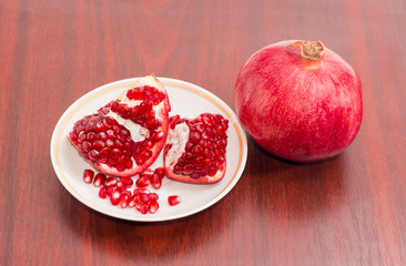 One whole pomegranate and peeled pomegranate on saucer