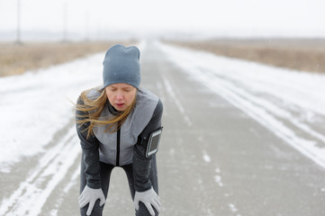 Tired woman having a rest after hard workout on a winter road.