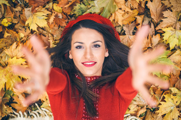 Portrait of a brunette woman laying in autumn leaves reaching out for a hug