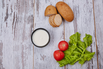 Sour cream, slliced bread, tomato, salad on rustic table