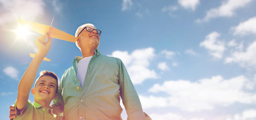 senior man and boy with toy airplane over sky