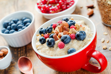 Oatmeal porridge with fresh blueberries, raspberries, muesli and almonds in red bowl. Healthy breakfast, healthy eating, vegan food concept. Colorful breakfast for kids, selective focus, close up