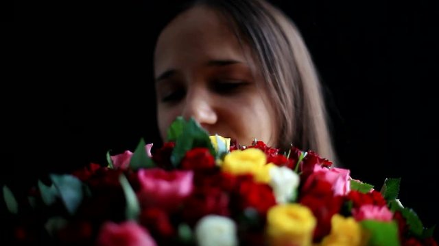 Beautiful woman with a large bouquet of flowers in her arms smelling a fragrant colorful roses on black background. 1920x1080
